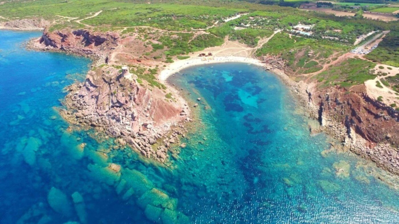 Vue aérienne d’une zone côtière avec une plage, un littoral rocheux et des eaux d’un bleu limpide.