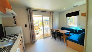 Una cocina compacta con estufa a gas, un comedor con mesa y sillas, un sofá azul y un ventanal corredizo que da a un patio exterior.