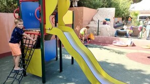 Une aire de jeux avec un toboggan jaune, des structures d’escalade et un mur d’escalade.