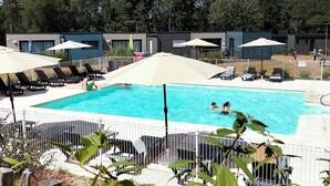 Ein Schwimmbecken mit Liegestühlen und Sonnenschirmen, umgeben von einem Zaun und Bäumen im Hintergrund.