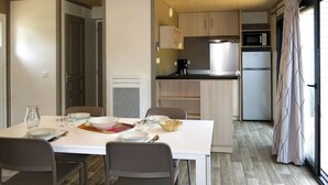 Eine kleine Küche mit modernen Geräten, ein Essbereich mit weißem Tisch und Stühlen sowie ein großes Fenster mit Vorhängen.