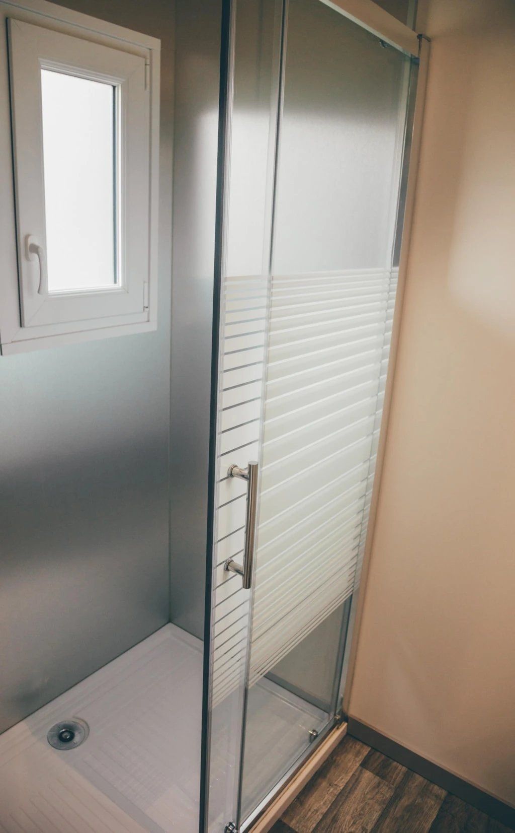 Ducha con cerramiento de cristal, puerta blanca y una ventana arriba.