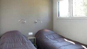 Une chambre avec deux lits, une fenêtre et un luminaire fixé au mur.