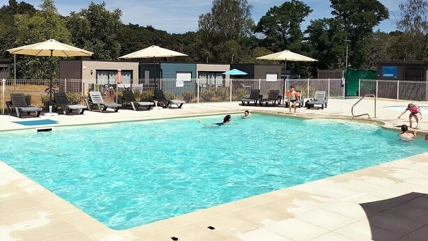 Une piscine entourée d’une clôture et d’arbres, avec des chaises longues et des parasols.