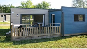 Une petite maison mobile d’un seul étage, dotée d’une terrasse et d’un espace extérieur aménagé et couvert.