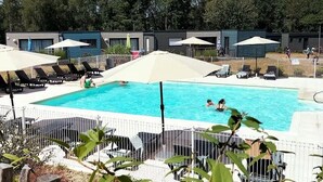 A swimming pool with lounge chairs and umbrellas, surrounded by a fence and trees in the background. - ZEcamping 3* piscine cottage TV LV 55m2 6 pers (Pluherlin)