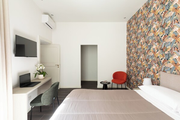 Una habitación de hotel moderna con una cama, un escritorio con una computadora portátil, una silla, un televisor y una pared con un llamativo estampado de hojas.