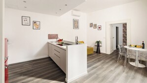 Een moderne keuken met een centraal eiland, een eetgedeelte met een ronde tafel en stoelen, en een gang die naar een andere kamer leidt.