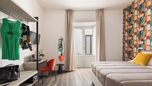 Een moderne hotelkamer met een bed, bureau, stoel en een kleurrijk abstracte muur.