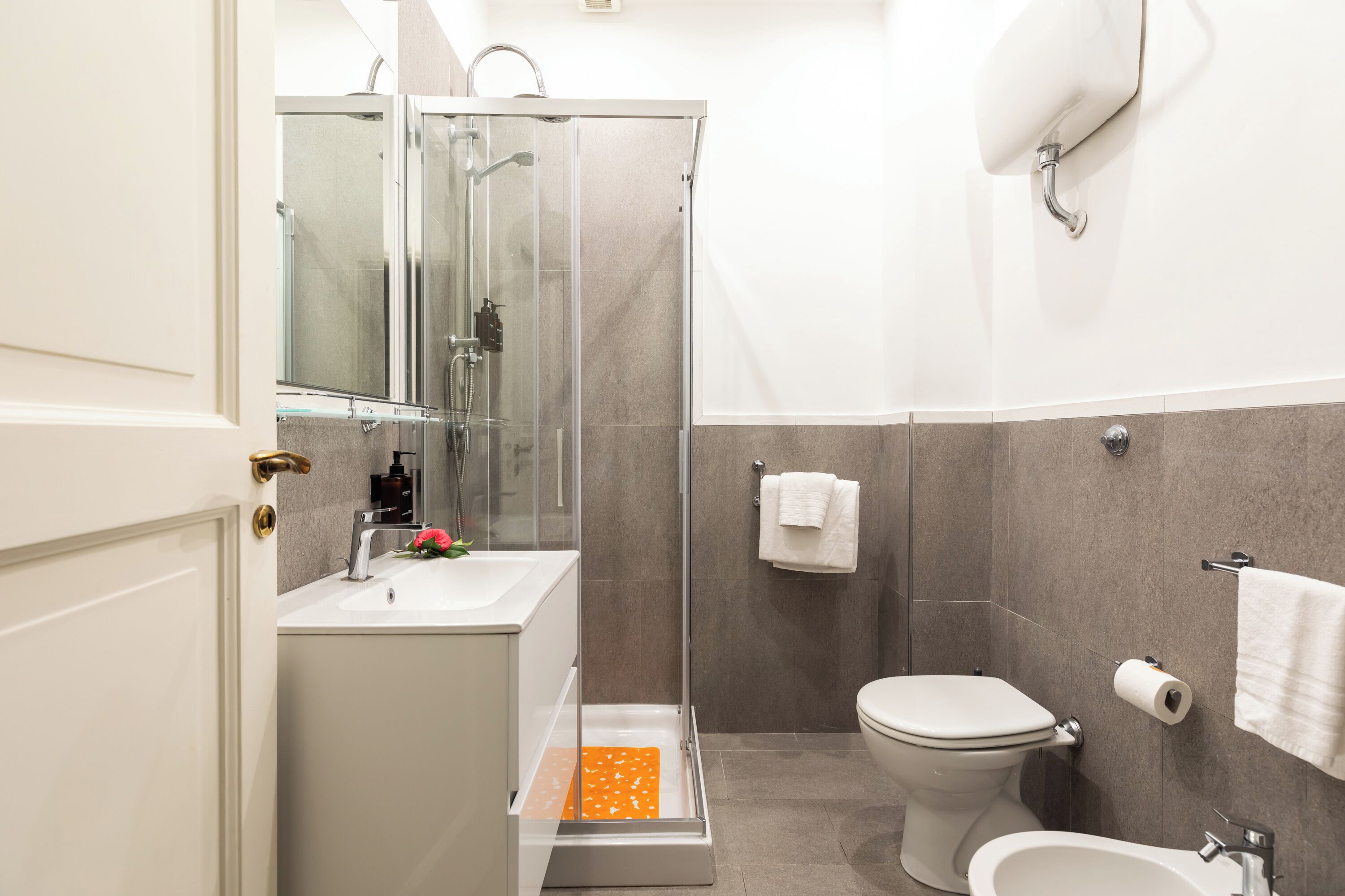 Een moderne badkamer met een douchecabine van glas, een toilet, een bidet en een wastafel.