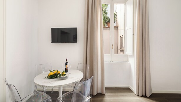 Een eethoek met een ronde tafel, transparante stoelen, een flatscreen televisie aan de muur en een raam met gordijnen.