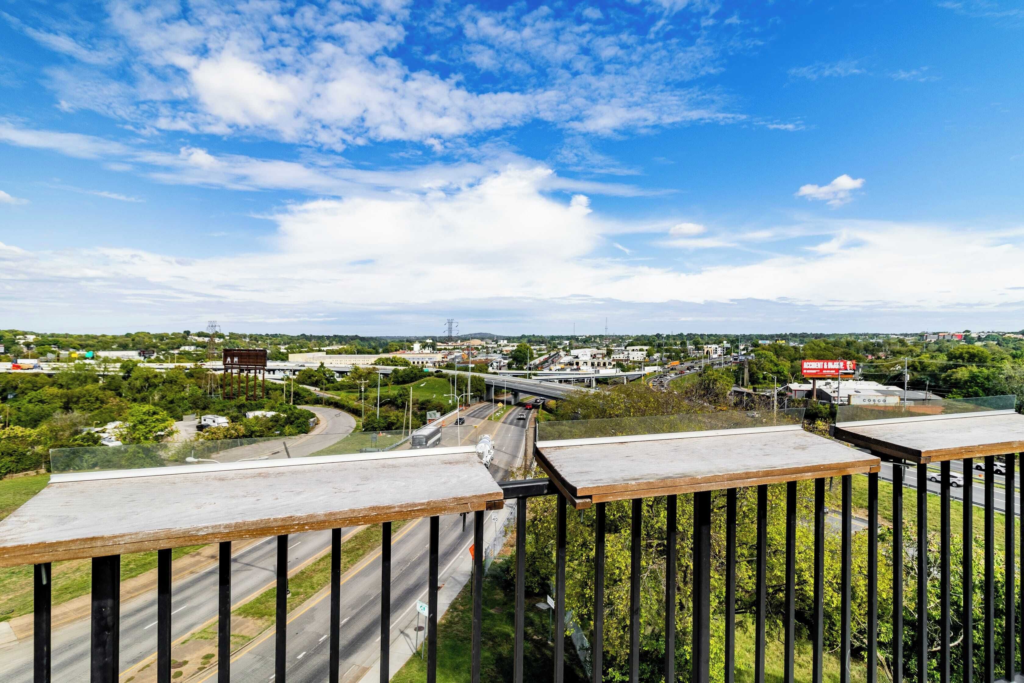 A high vantage point overlooking a cityscape with a highway, greenery, and a clear sky.