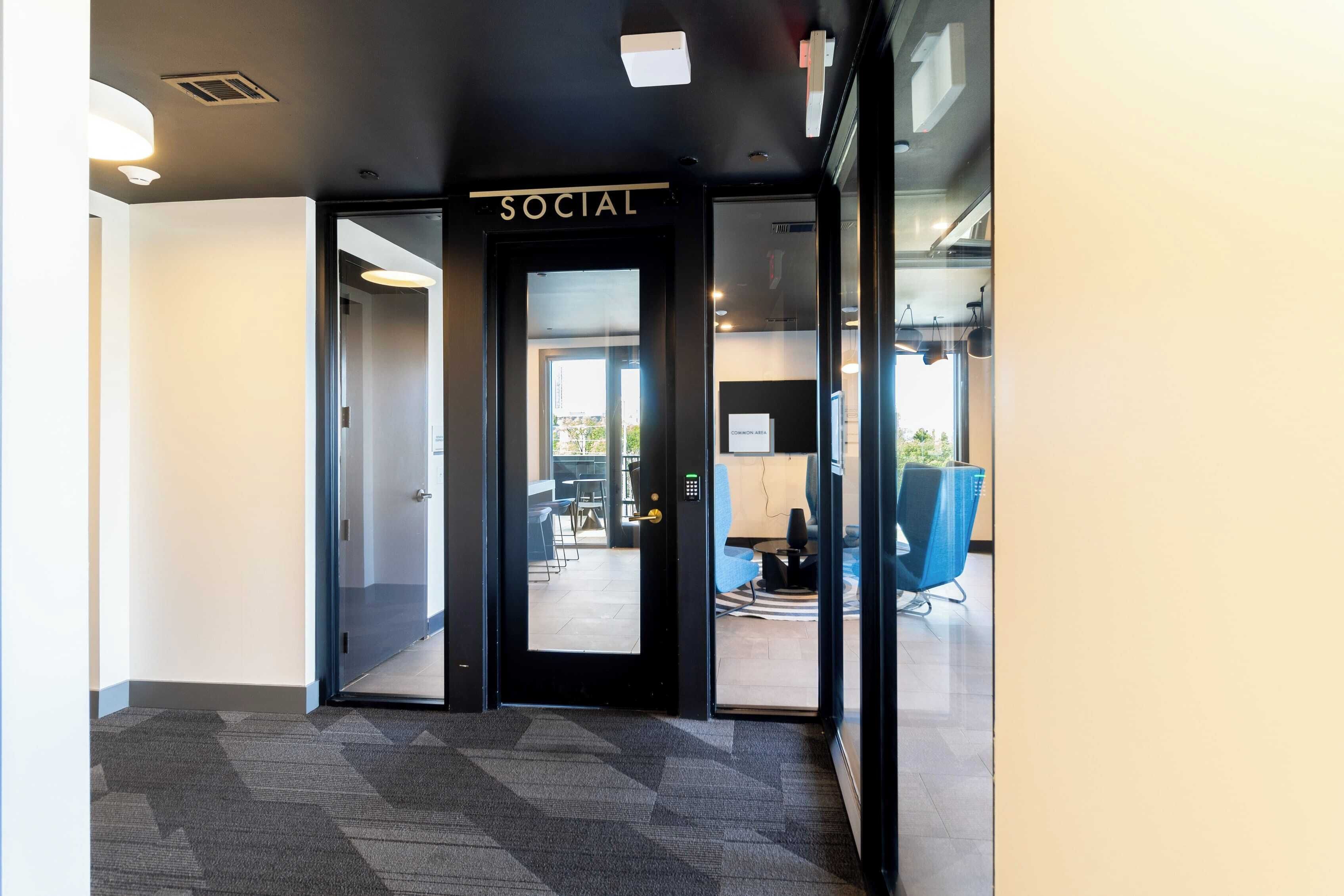 A modern office entrance with a 'SOCIAL' sign, a glass door, and a view into a well-lit interior space with seating.