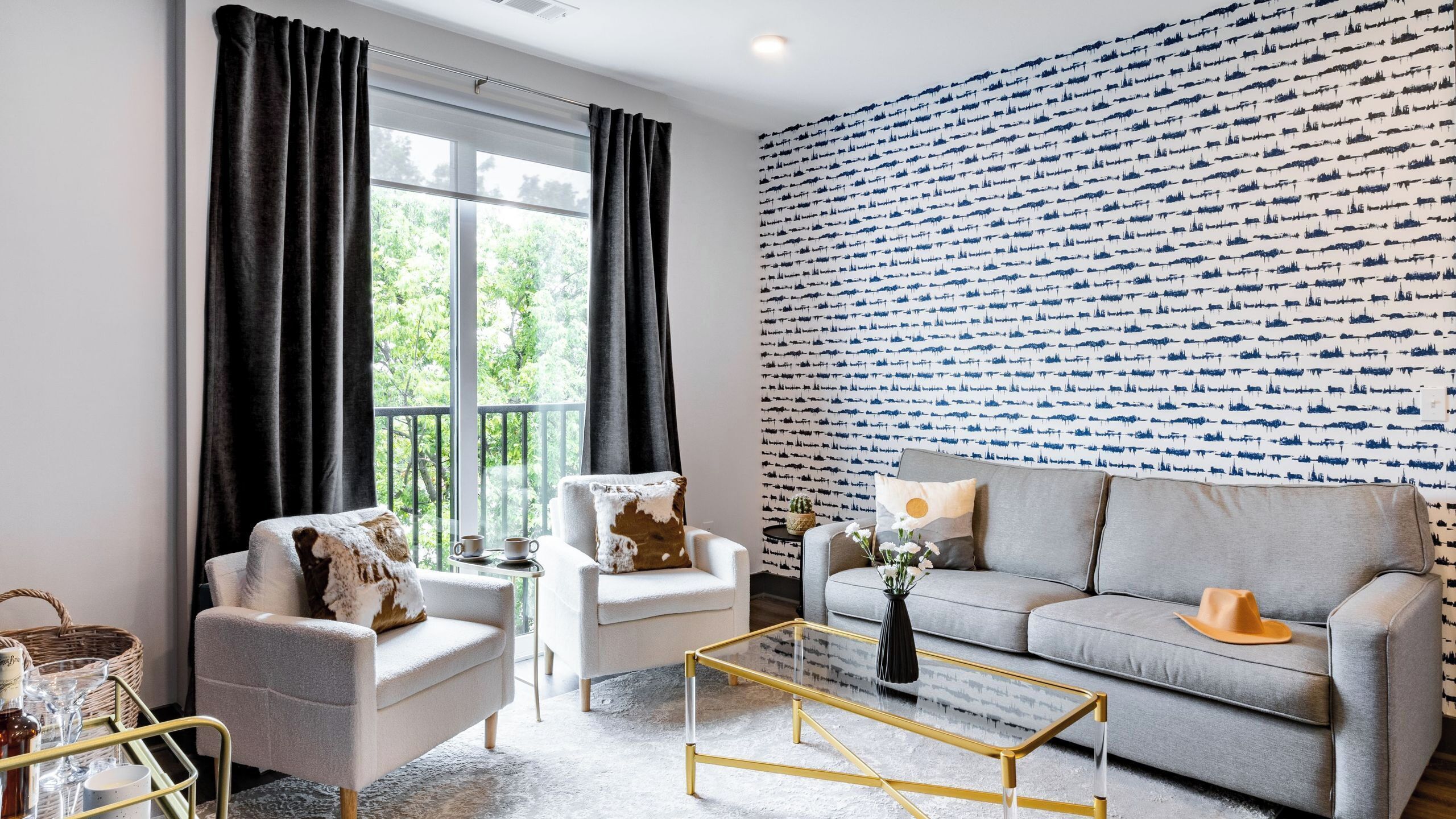 A modern living room with a grey sofa, a white armchair, a glass coffee table, and a patterned wall.