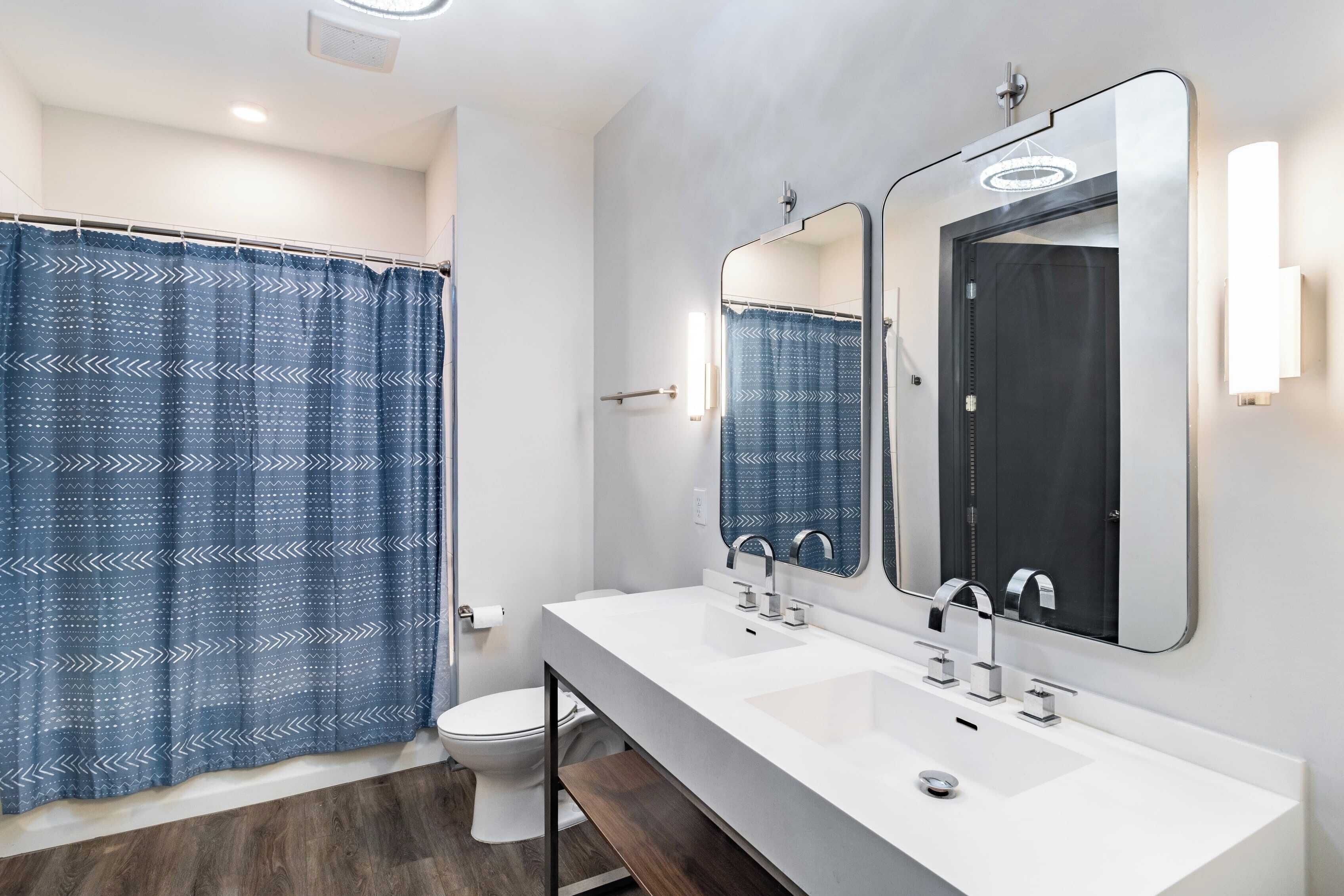 Un baño moderno con cortina de ducha, dos lavamanos y un inodoro.