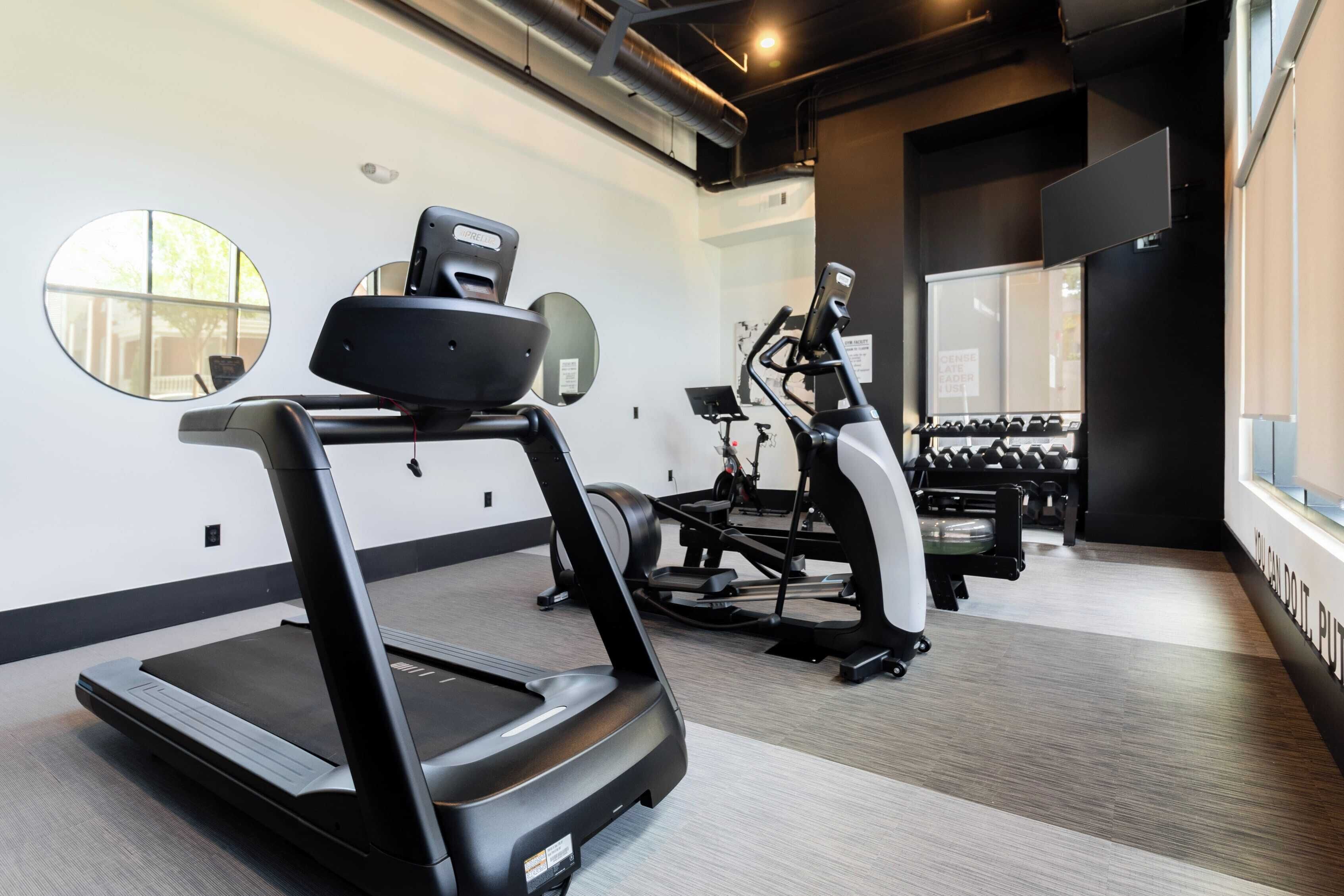 A modern gym with treadmills, elliptical machines, and dumbbells.