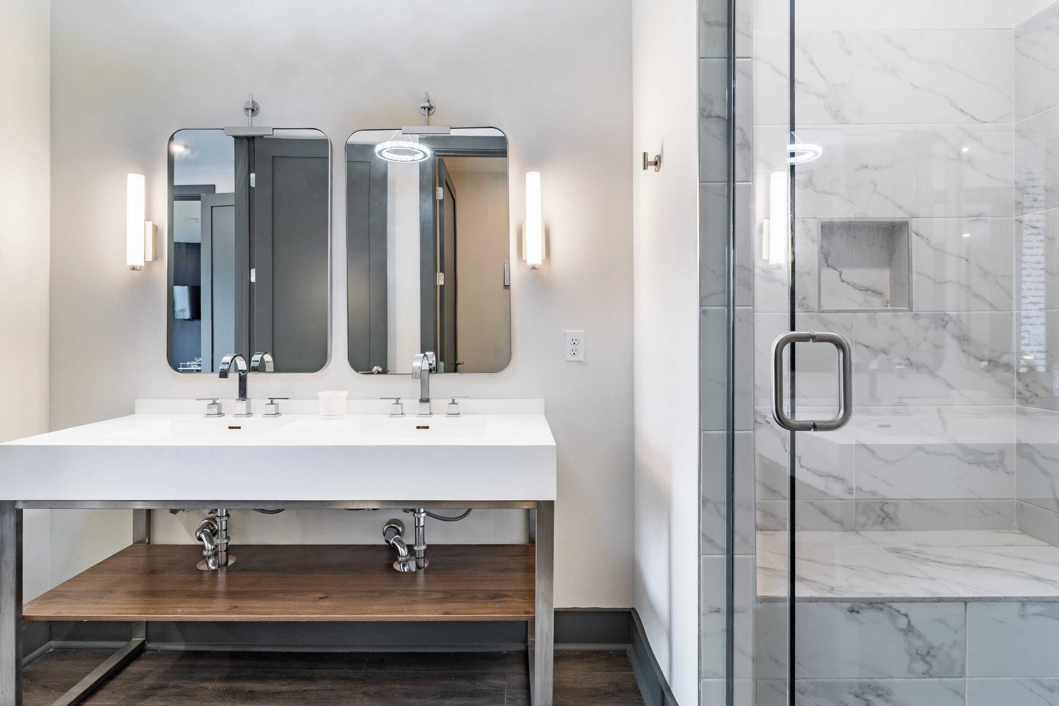 A modern bathroom with a white sink, two mirrors, and a glass shower enclosure.