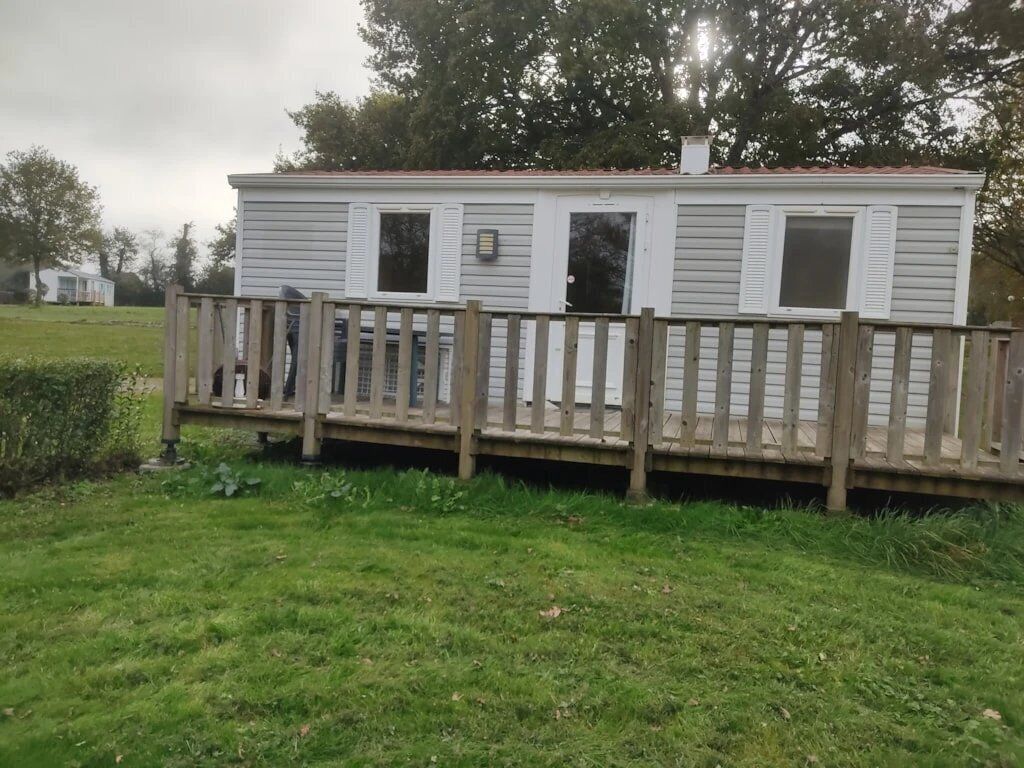 A mobile home with a wooden deck and a fenced area.