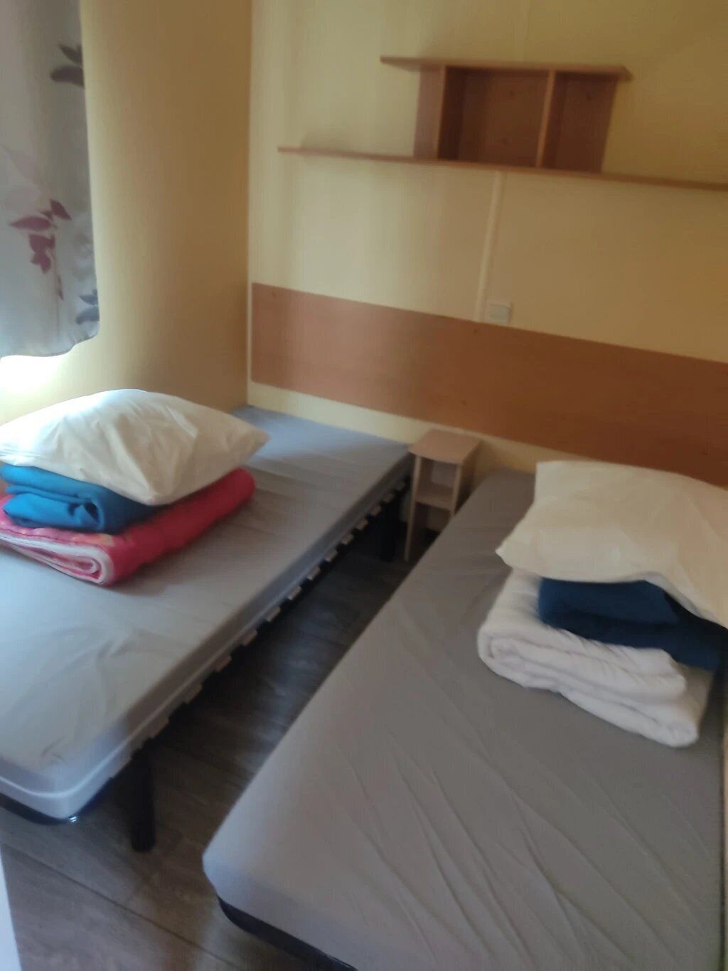 Habitación de hotel con dos camas, cada una con un colchón y almohadas. Hay un pequeño estante de madera sobre las camas.