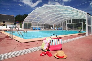 Ein Swimmingpool mit einem verglasten Bereich, Liegestühlen und einer Poolanlage mit einer Tasche und Flip-Flops.