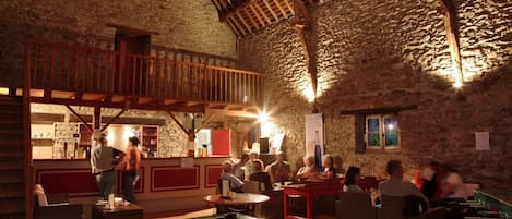 Una sala de billar con mesa de pool, vigas de madera, paredes de piedra y barandilla roja.