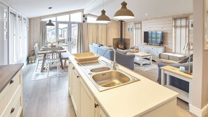 A modern kitchen with a central island, a dining area with a table and chairs, a sofa, and a TV. - Host Stay Puffin s Rest (Saltburn-by-the-Sea)