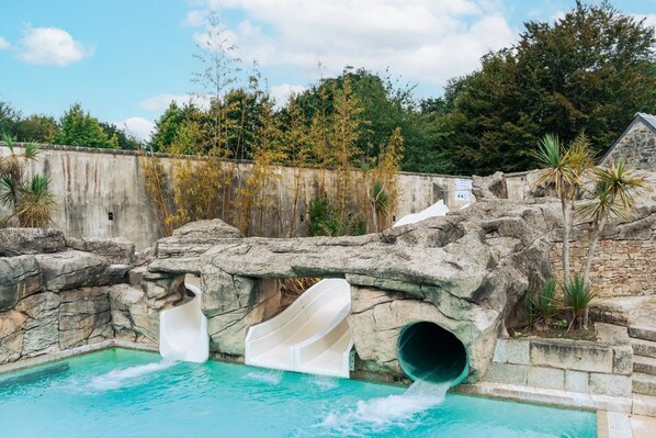 A pool with slides and a rocky wall.