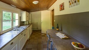 A kitchen with a wooden ceiling, a window, a sink, a microwave, a radiator, a bottle of wine, and a fruit bowl. - ZEcamping 5 étoiles parc aquatique tente TV LV BBQ 116m2 (Quimper)
