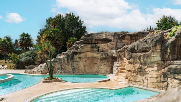 A pool area with multiple swimming pools, a rocky backdrop, and surrounding greenery. - ZEcamping 5 étoiles parc aquatique tente TV LV BBQ 116m2 (Quimper)