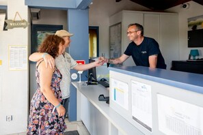 Un comptoir d’accueil avec une pancarte « BIENVENUE », un ordinateur et des affiches d’information.