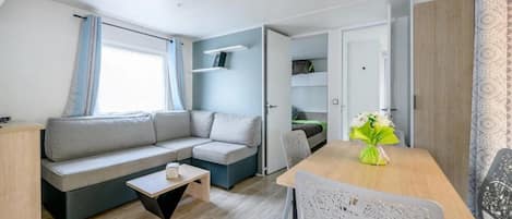 A compact living space with a sofa, a small table, a chair, and a bed in the background.