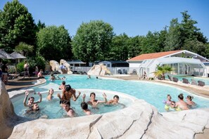 A swimming pool with rock formations and a covered area with chairs.