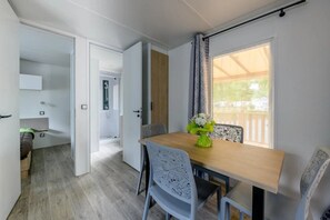 A modern room with a wooden dining table, two chairs, a small vase with flowers, and a window with curtains.