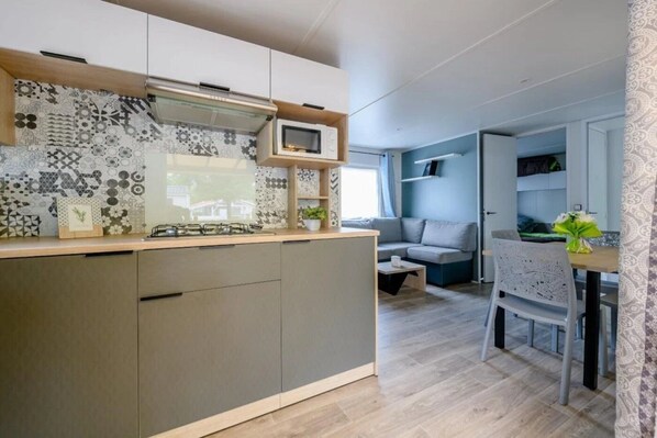 A compact kitchenette with a microwave, stove, and storage cabinets. There is a dining area with a table and chairs, and a sofa in the background.