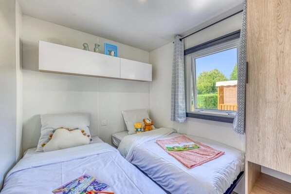 Une chambre avec deux lits, une fenêtre avec des rideaux et une étagère ornée d’objets décoratifs.