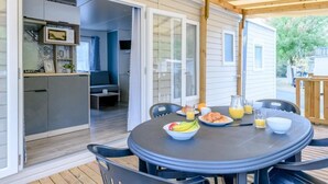Une terrasse couverte avec une table ronde mise pour le petit-déjeuner, comprenant des assiettes de fruits et des jus.