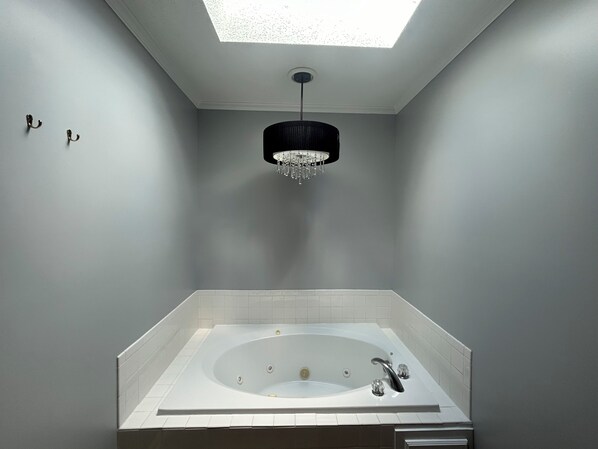 A modern bathroom with a freestanding bathtub, a skylight, and a chandelier.