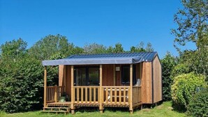 En træhytte med veranda, omgivet af grøn vegetation.