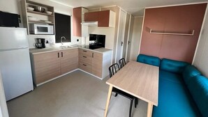 A compact kitchen with a microwave, sink, and cabinets, a dining table, and a blue sofa.