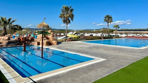 A swimming pool area with multiple pools, palm trees, and a clear blue sky.
