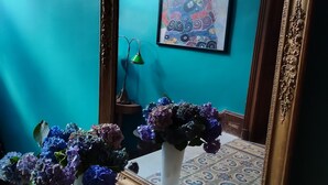 A room with a teal wall, a framed painting, a vase with purple flowers, a green lamp, and a patterned floor. - Suite de Charme en Mezzanine (Remiremont)