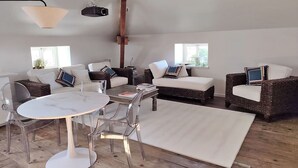 A spacious living area with a round table, clear chairs, and two sofas. - Suite de Charme en Mezzanine (Remiremont)