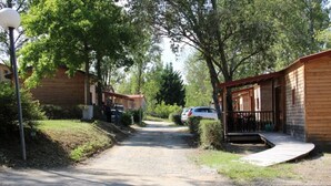 A gravel path leading to wooden cabins with a covered porch, surrounded by trees and greenery.