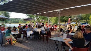 An outdoor dining area with tables and chairs under a canopy, overlooking a body of water.