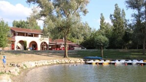 A lakeside building with a red-tiled roof, a stone pathway, and a row of small boats docked along the water's edge.