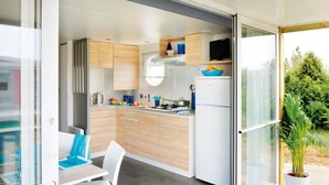 A compact kitchen with wooden cabinets, a microwave, and a refrigerator. - ZEcamping 3 étoiles piscine animations locatif TV LV clim 33m2 4 pers (Nailloux)