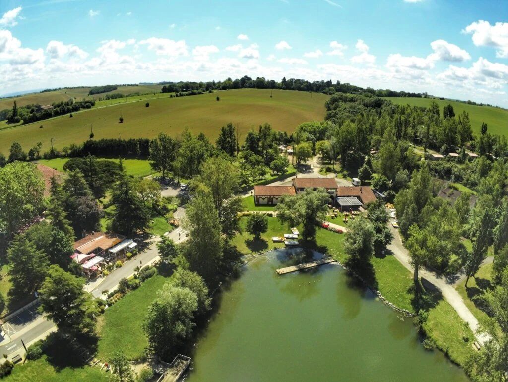 An aerial view of a rural property with a large pond, surrounding greenery, and a few buildings.