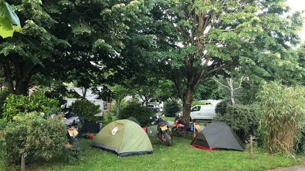 Un camping con dos tiendas de campaña, una motocicleta y un automóvil estacionado cerca.