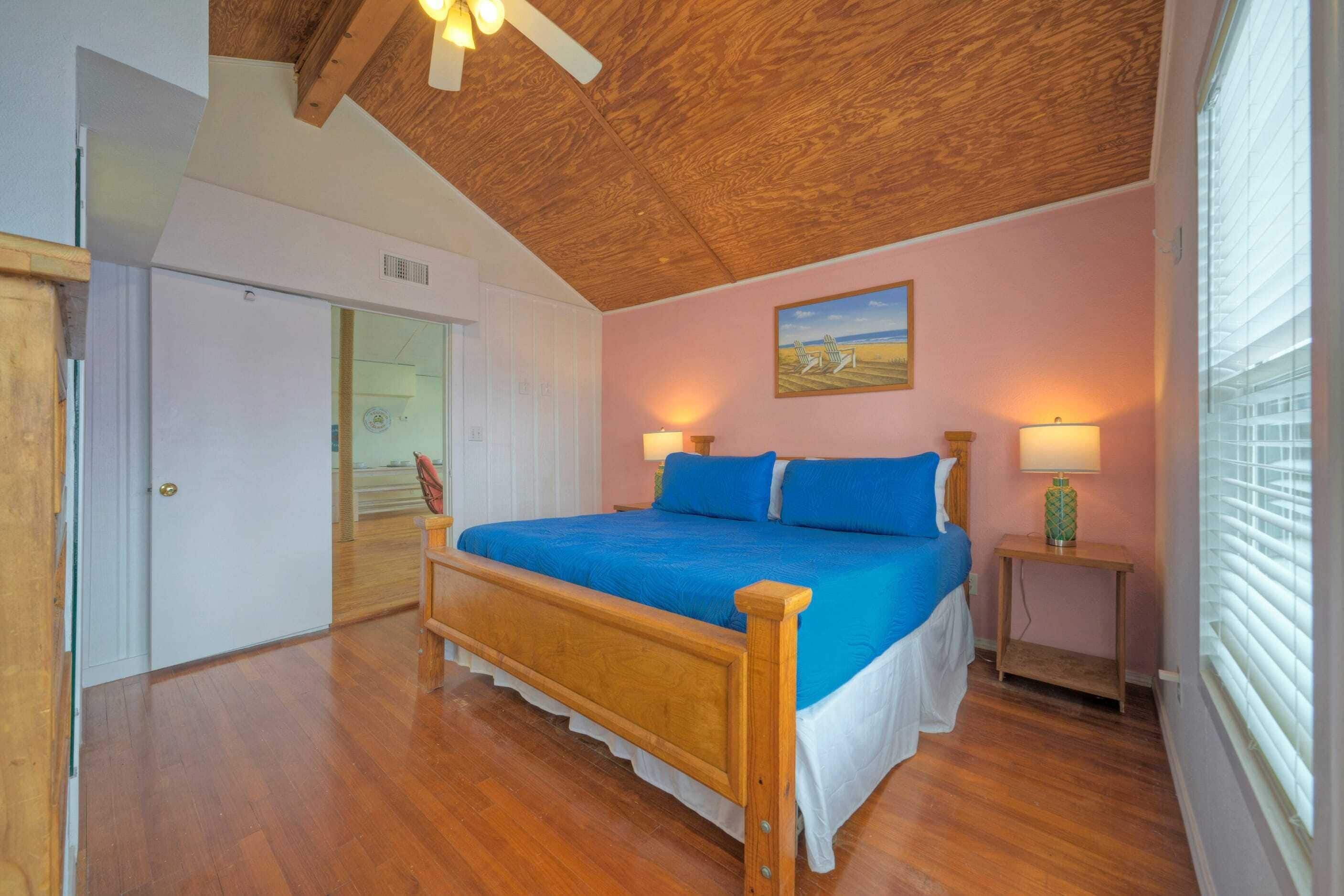 Un dormitorio con una cama de madera, un cuadro en la pared y una ventana con persianas.