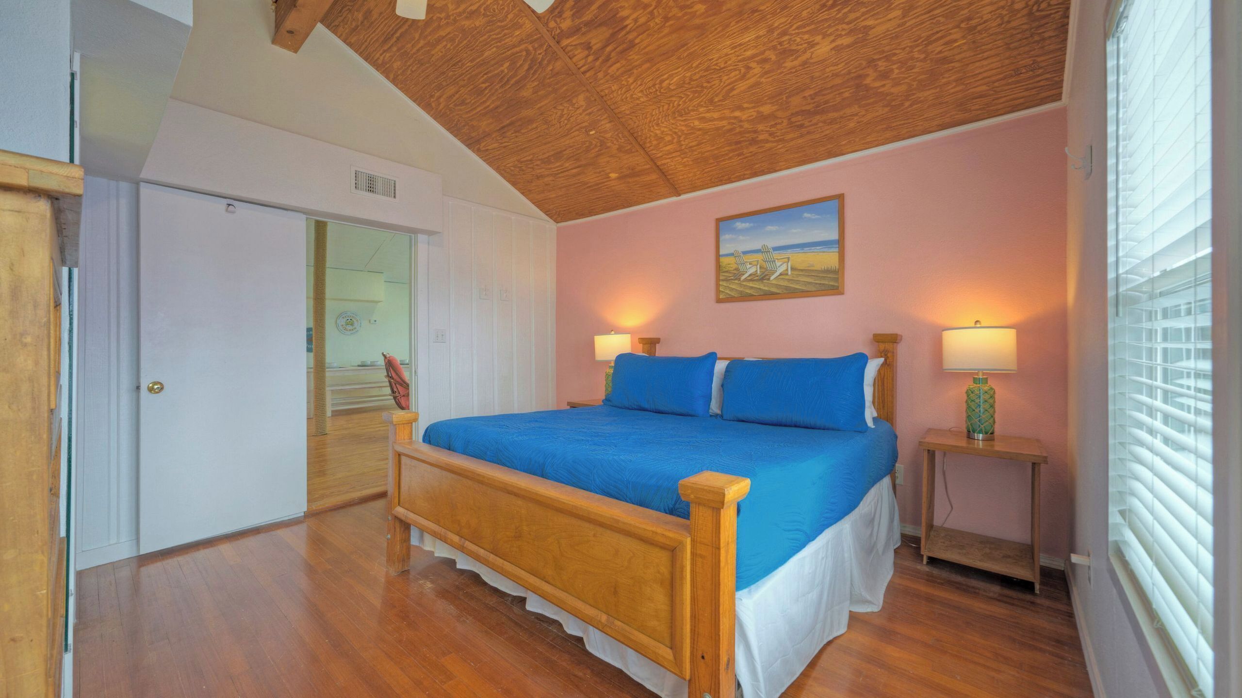 A bedroom with a wooden bed, a painting on the wall, and a window with blinds.